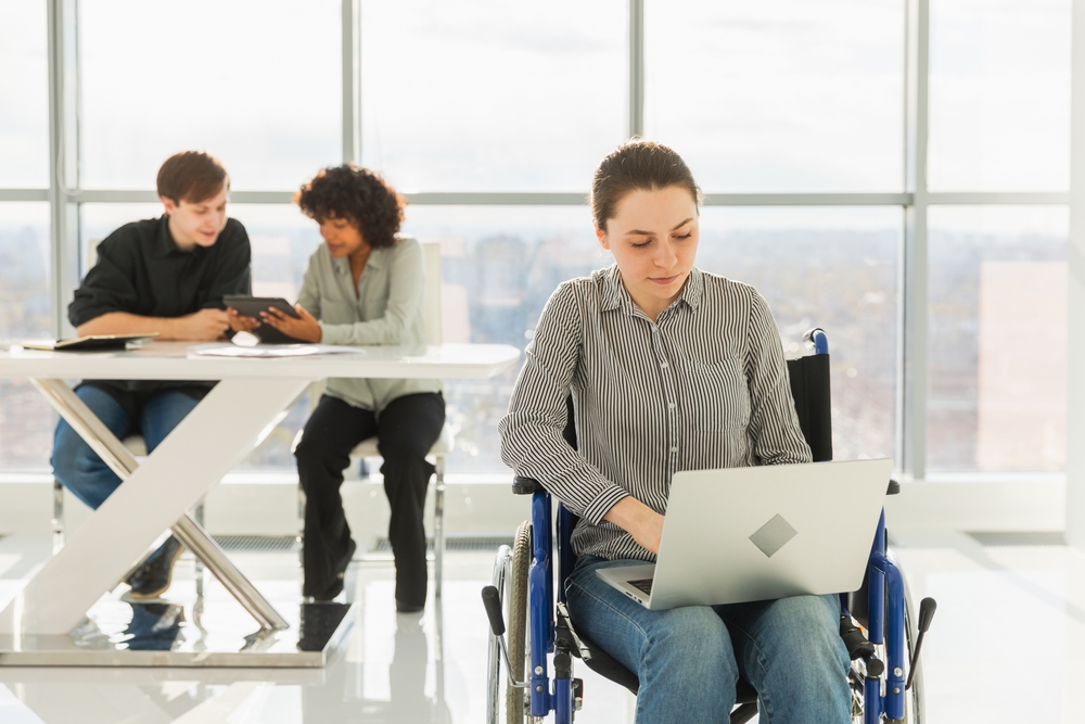 Accessible environment. Woman in chair for people with disability working with laptop in modern office